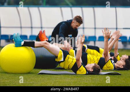 Gruppo di giocatori di calcio in formazione di fisioterapia. Young Trainer offre consigli ai giocatori su allenamenti e stretching agility. Allenare il calcio in Teen Foto Stock