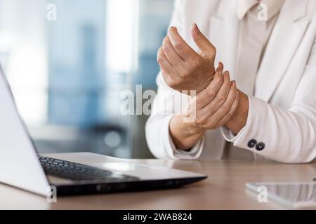 Una foto ravvicinata delle mani di una donna d'affari anziana seduta in ufficio a una scrivania, che massaggia la mano stanca. Foto Stock