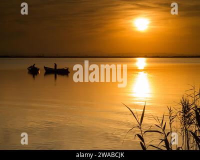 Due barche sul lago del parco naturale Albufera a Valencia al tramonto con il sole vicino all'orizzonte Foto Stock