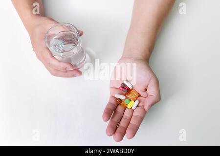 Vista dall'alto di pillole colorate, medicine in capsula e un bicchiere d'acqua nelle mani dell'uomo. Trattamento di COVID-19 a casa secondo le raccomandazioni del medico. Foto Stock