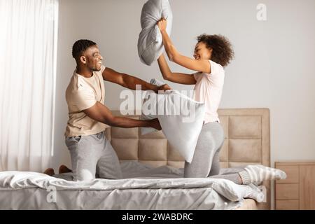 La giovane coppia nera si impegna giocherellamente in una lotta con i cuscini al chiuso Foto Stock