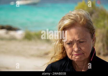 Ritratto ravvicinato di una donna triste e matura in una spiaggia ventosa che guarda in basso Foto Stock