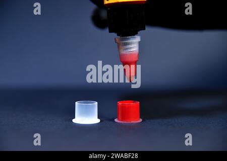 Gocciolamento di inchiostro rosso in una piccola tazza di plastica. Concetto di arte e design. Primo piano Foto Stock