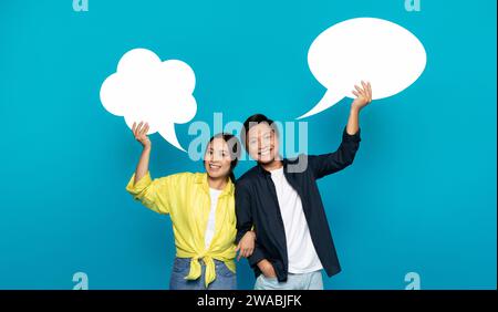 Una coppia asiatica esuberante regge con gioia bolle di discorso, simboleggiando una conversazione vivace Foto Stock