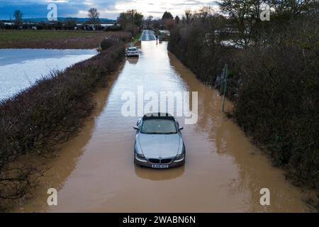 Offenham, Evesham, 3 gennaio 2024 - Un pilota BMW ha provato e non è riuscito a guidare attraverso le acque alluvionali nonostante un altro veicolo già abbandonato sullo stesso tratto. L'anziano pilota ha fatto girare il motore mentre guidava, ma la sua velocità era troppo elevata e l'acqua è entrata nel motore. Il veicolo alla fine ripartì, ma si divise in un'altra fermata a pochi metri dalla terraferma. Un lavoratore stradale è arrivato e ha messo un cartello "strada chiusa" davanti al suo veicolo come insulto finale. È successo vicino al parco caravan di Offenham, vicino a Evesham nel Worcestershire, dove il fiume Avon ha brecce Foto Stock