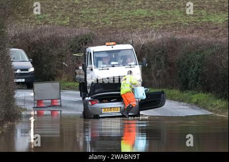 Offenham, Evesham, 3 gennaio 2024 - Un pilota BMW ha provato e non è riuscito a guidare attraverso le acque alluvionali nonostante un altro veicolo già abbandonato sullo stesso tratto. L'anziano pilota ha fatto girare il motore mentre guidava, ma la sua velocità era troppo elevata e l'acqua è entrata nel motore. Il veicolo alla fine ripartì, ma si divise in un'altra fermata a pochi metri dalla terraferma. Un lavoratore stradale è arrivato e ha messo un cartello "strada chiusa" davanti al suo veicolo come insulto finale. È successo vicino al parco caravan di Offenham, vicino a Evesham nel Worcestershire, dove il fiume Avon ha brecce Foto Stock