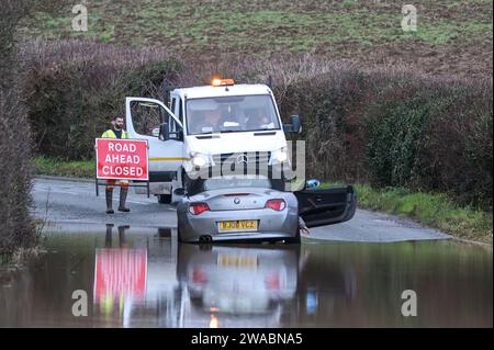 Offenham, Evesham, 3 gennaio 2024 - Un pilota BMW ha provato e non è riuscito a guidare attraverso le acque alluvionali nonostante un altro veicolo già abbandonato sullo stesso tratto. L'anziano pilota ha fatto girare il motore mentre guidava, ma la sua velocità era troppo elevata e l'acqua è entrata nel motore. Il veicolo alla fine ripartì, ma si divise in un'altra fermata a pochi metri dalla terraferma. Un lavoratore stradale è arrivato e ha messo un cartello "strada chiusa" davanti al suo veicolo come insulto finale. È successo vicino al parco caravan di Offenham, vicino a Evesham nel Worcestershire, dove il fiume Avon ha brecce Foto Stock