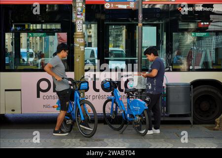 Barcellona, Spagna - 26 maggio 2022: Due adolescenti di origine asiatica stanno per utilizzare il servizio di biciclette elettriche utilizzando l'applicazione per telefono cellulare. Foto Stock