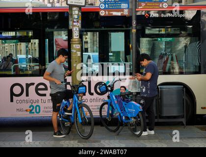 Barcellona, Spagna - 26 maggio 2022: Due adolescenti di origine asiatica stanno per utilizzare il servizio di biciclette elettriche utilizzando l'applicazione per telefono cellulare. Foto Stock