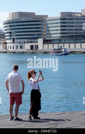 Barcellona, Spagna - 26 maggio 2022: Giovane rossa con i capelli raccolti fotografa il paesaggio portuale, mentre il suo partner guarda al World Trade Center B. Foto Stock