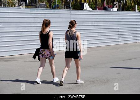 Barcellona, Spagna - 26 maggio 2022: Due giovani donne con i capelli legati alla schiena e gli occhiali da sole camminano insieme con bottiglie d'acqua nelle mani attraverso la t Foto Stock