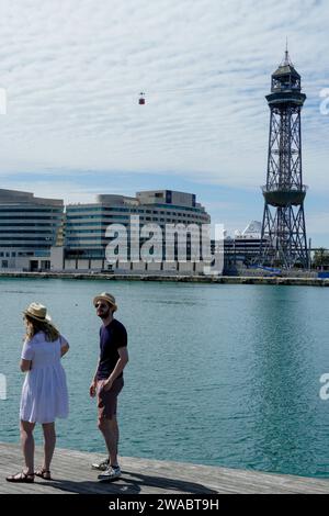 Barcellona, Spagna - 26 maggio 2022: Una coppia visita il porto di Barcellona, con cappelli estivi, una funivia attraversa il cielo delle nuvole bianche. Foto Stock