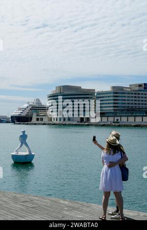 Barcellona, Spagna - 26 maggio 2022: La coppia con cappello estivo prende un autoritratto vicino alla scultura di un uomo che guarda verso le stelle di Robert Llimos i. Foto Stock