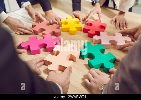 Gli uomini d'affari mettono puzzle colorati sul desktop e presentano il concetto di cooperazione aziendale, lavoro di squadra, supporto e assistenza in ufficio. Foto Stock