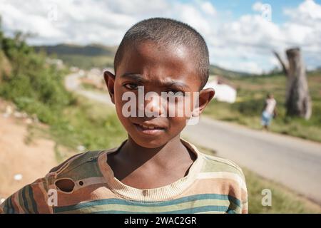 Ivato, Madagascar - 26 aprile 2019: Giovane ragazzo malgascio sconosciuto che indossa una vecchia camicia strappata donata dai turisti, in posa per la macchina fotografica - gente del Madagascar ar Foto Stock