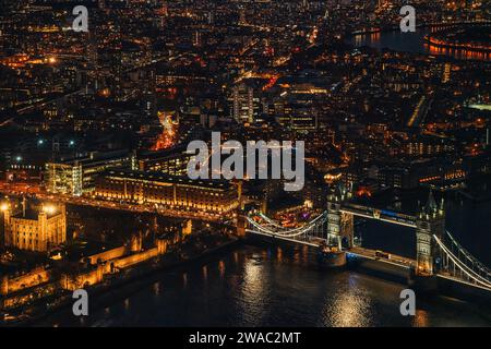Vista aerea notturna del Tower Bridge sul fiume Tamigi, edifici illuminati che illuminano al buio Foto Stock