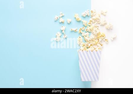 Un secchiello a righe di popcorn su sfondo bianco e azzurro, vista dall'alto e spazio di copia. Foto Stock