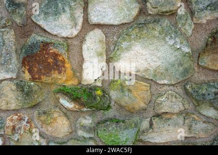 Un vecchio muro irregolare del giardino con muschio e alghe ricoperte. Foto Stock