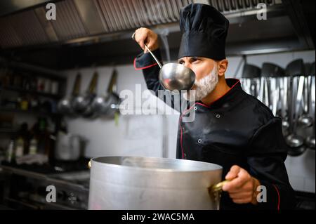 Lo chef assaggia una zuppa da un mastol Foto Stock