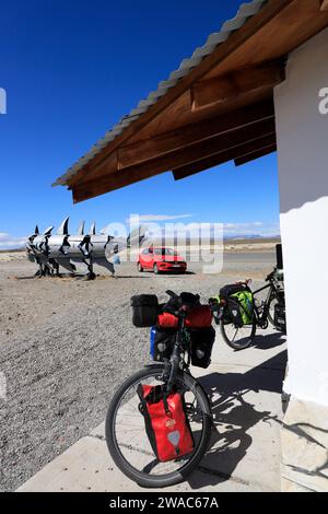 Parcheggio biciclette all'esterno di un riparo lungo la strada con la scultura di pesce metallico vicino all'incrocio tra la RN 40 e la RP23 sulla RP23 sulla strada per El Chalten sullo sfondo.Patagonia.Provincia di Santa Cruz.Argentina Foto Stock