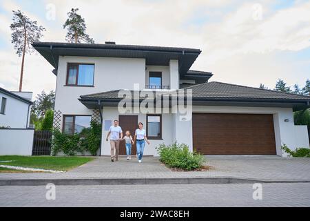 Felice famiglia caucasica che si tiene per mano e corre da una nuova casa cittadina moderna Foto Stock