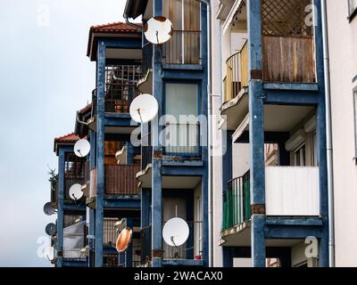 Piatti satellitari montati sui balconi di un grande edificio di appartamenti. Tecnologia per ricevere i canali tv. Il quartiere residenziale sembra essere povero. Foto Stock