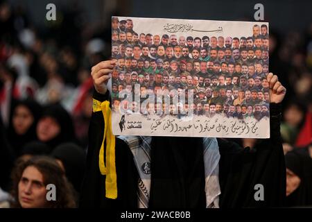 Beirut, Libano. 3 gennaio 2024. Un sostenitore pro-iraniano di Hezbollah solleva un poster che mostra tutti i militanti di Hezbollah che sono stati uccisi dopo l'attacco a sorpresa di Hamas su Israele il 07 ottobre durante una messa come Segretario generale di Hezbollah Hassan Nasrallah sembra tenere un discorso televisivo per celebrare il quarto anniversario dell'assassinio di Abu Mahdi al-Mohandes, vice capo della milizia irachena di Hashd al-Shaabi, e comandante della forza Quds iraniana Qasem Soleiman da un drone statunitense in Iraq nel 2020. Crediti: Marwan Naamnai/dpa/Alamy Live News Foto Stock