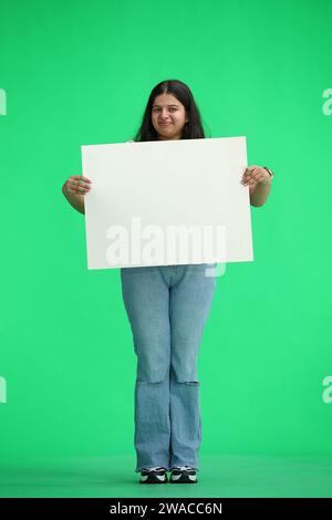 Una donna, su sfondo verde, a piena altezza, con un foglio bianco Foto Stock