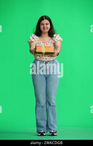 Una donna, su sfondo verde, a piena altezza, con un dono Foto Stock