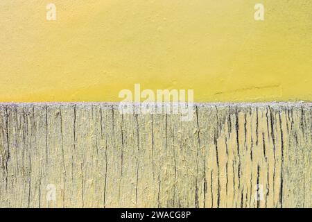 Primo piano di una parete di legno incrinata e intemprata e di una parete di cemento intonacato dipinta di giallo chiaro e luminoso. Sfondo con texture astratta, spazio di copia. Foto Stock