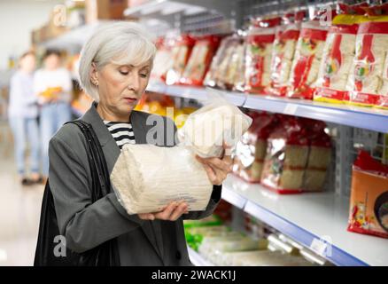 Signora anziana interessata che legge etichetta su confezioni di noodles asiatici nel supermercato Foto Stock