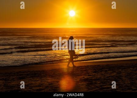 Silhouette di donna che cammina lungo Cannon Beach Foto Stock