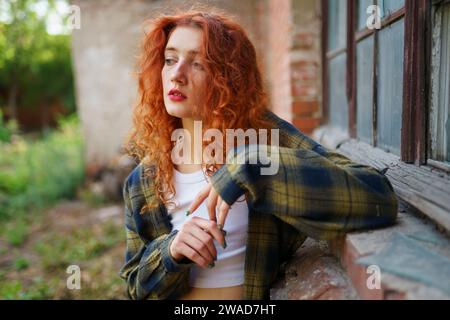 Donna dai capelli rossi in posa accanto alla vecchia casa dei mattoni Foto Stock