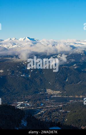 Una vista spettacolare della vallata di Whistler Village e del Green Lake sullo sfondo di pendii di montagna boscosi e cime innevate inghiottite dalle nuvole Foto Stock