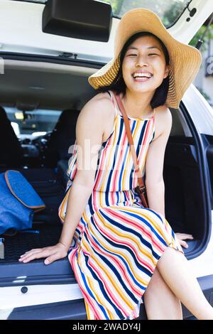 Ritratto di donna asiatica felice seduta in macchina e con cappello da sole in giardino a casa. Vita domestica, estate e stile di vita, inalterato. Foto Stock