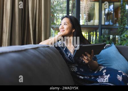 Donna asiatica premurosa sul divano che usa un tablet a casa. Vita domestica, tecnologia e stile di vita, inalterati. Foto Stock