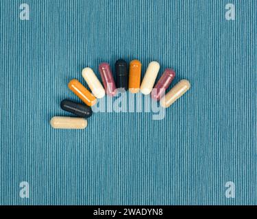 Vista dall'alto di una varietà di integratori vitaminici e minerali in capsule. Pillole multicolori in arancione e rosso su sfondo blu. Foto Stock