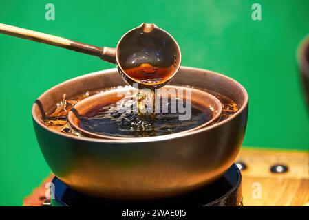 La tradizionale pentola di rame cinese serve tè PU'er, mentre il tè viene preparato intorno al piano cottura Foto Stock