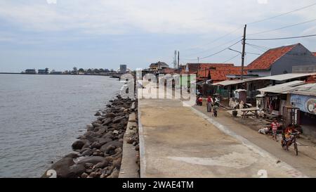 Un gruppo di bambini in bicicletta vicino a un argine costiero che mantiene le onde mareali a Pekalongan, Indonesia. Foto Stock