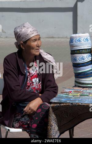 Un'anziana seduta in una strada che vende souvenir e cappelli in una giornata di sole Foto Stock