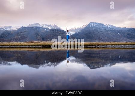 Una donna si trova all'esterno nella neve, tenendo un ombrello blu di fronte a una catena montuosa con cime innevate Foto Stock