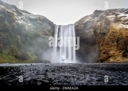 Un individuo sagomato si erge in primo piano su una maestosa cascata, illuminata da un cielo nuvoloso e coperto Foto Stock