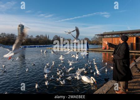 Man Feeding Birds il giorno di Santo Stefano, inverno, lago Serpentine a Hyde Park, Londra, Regno Unito Foto Stock