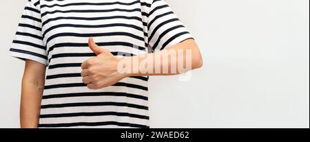 Una donna irriconoscibile in t-shirt a righe con i pollici verso l'alto. Riconoscimento, approvazione. Foto Stock