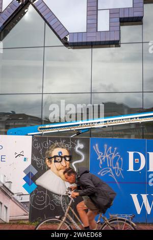 Ciclista che passa la nuova costruzione di un edificio multifunzionale chiamato 'huis van Delft' nei colori delftware nel centro della città di Delft Foto Stock