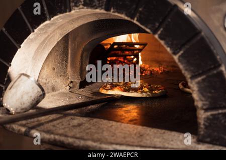 Cottura della pizza in un forno a legna in mattoni vecchio stile Foto Stock