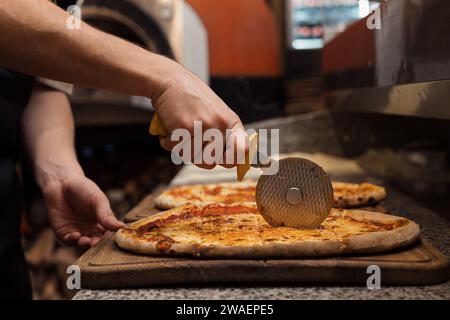 Primo piano dello chef che taglia la pizza calda su una tavola di legno Foto Stock