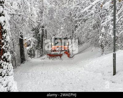 Spazzaneve giallo pulisce la neve su una strada di montagna Foto Stock