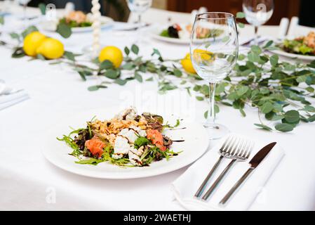 Un'insalata fresca e luminosa servita splendidamente su un piatto bianco in un elegante evento gastronomico, con un tavolo di gusto e accenti di limone. Foto Stock