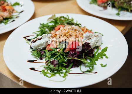 Insalata gourmet preparata con salmone affumicato, verdure miste e ciambelle di formaggio cremoso, condite con riduzione balsamica. Foto Stock